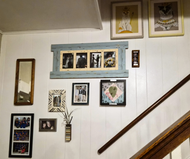 A collection of photos on a wall in a stairwell.  The shadow box is hanging there as well.  There are also two large framed portraits of cats as royalty.  The portraits were a birthday present from my wife.